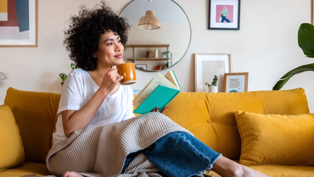 woman sips coffee on yellow couch min